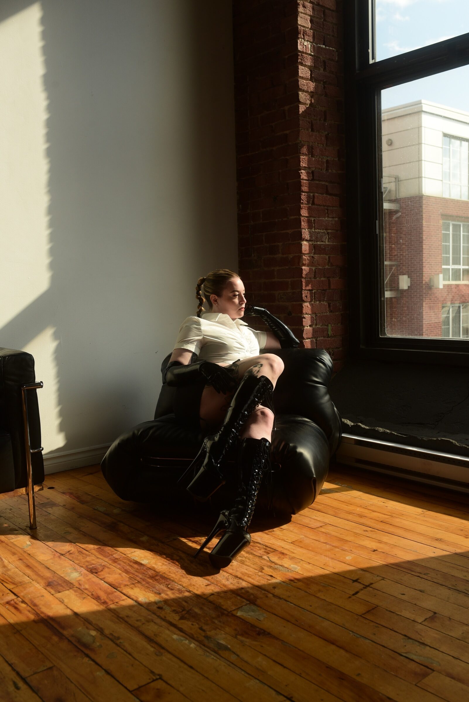 Louise assise dans un fauteuil noir baigné de lumière naturelle