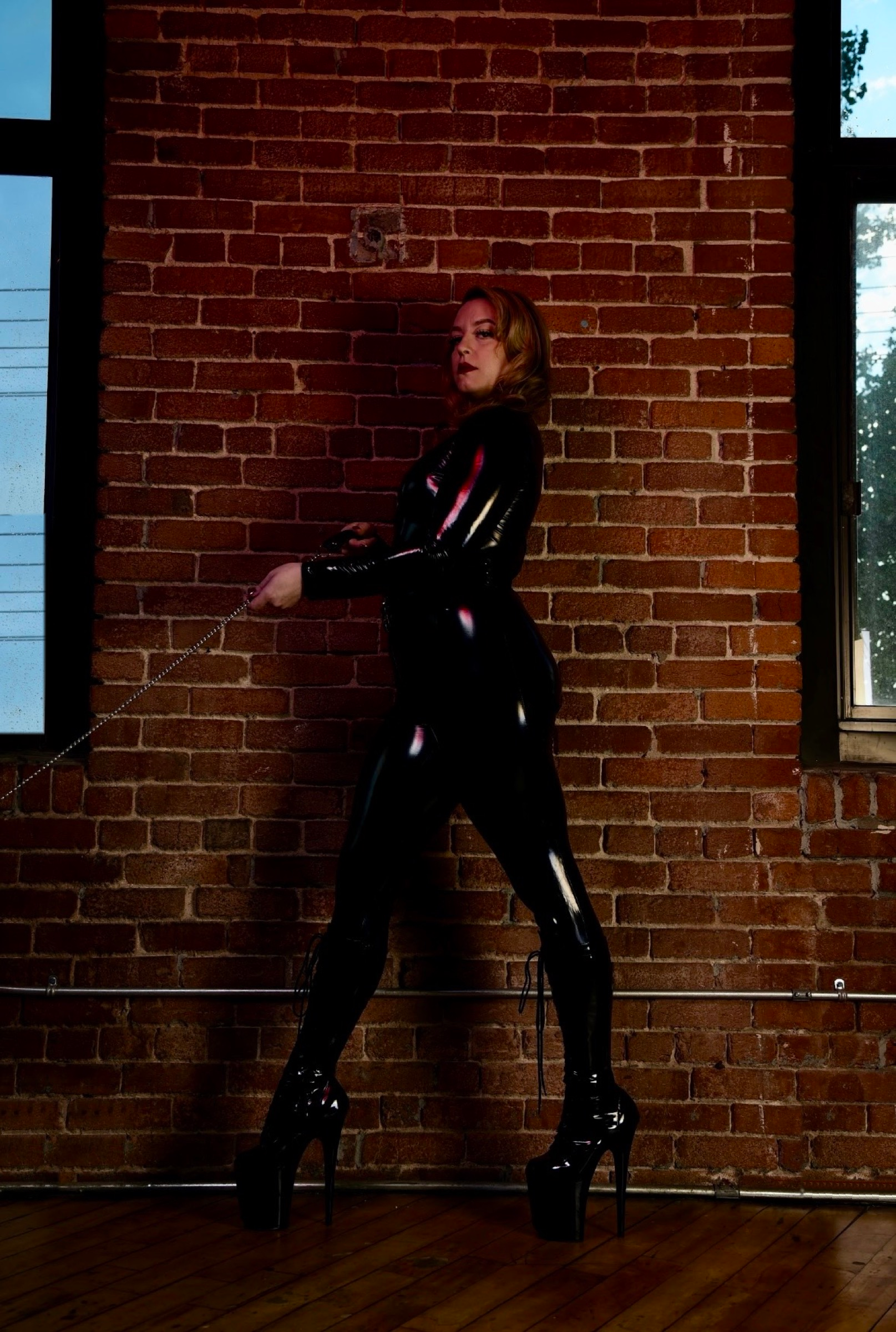 Louise en latex devant un mur de brique